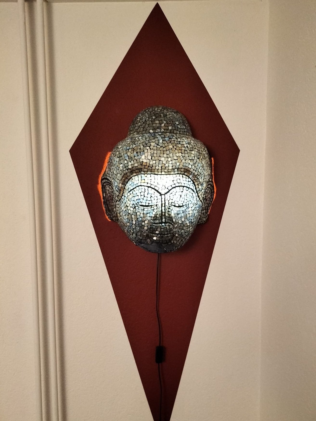 Dekorative Maske vor roter Rautenfläche an der Wand